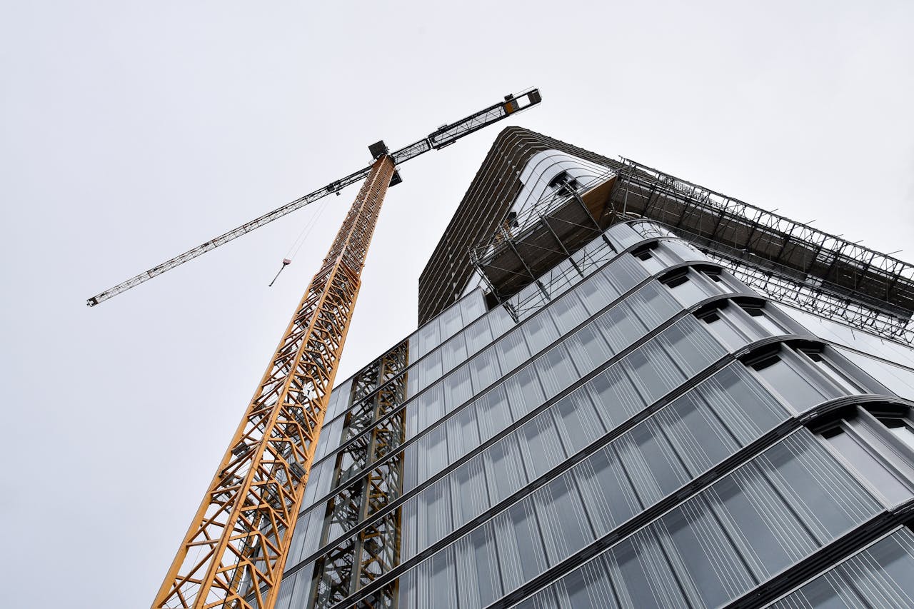 gallery-1 A low angle shot of modern building under construction with a crane viewed against the sky.