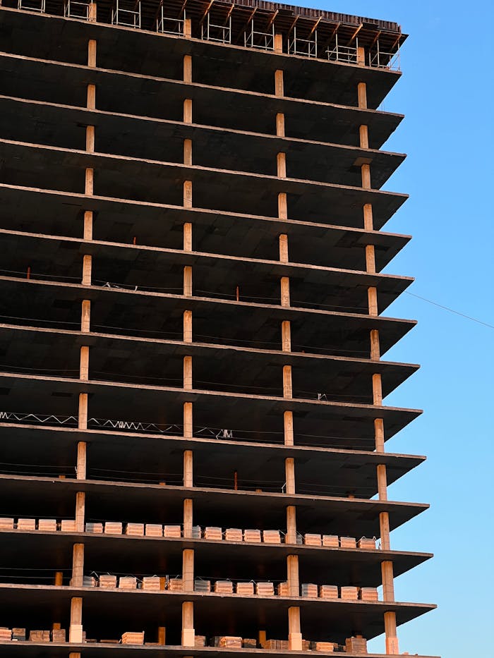 about-img Modern high-rise building under construction, showcasing concrete layers and blue sky backdrop.