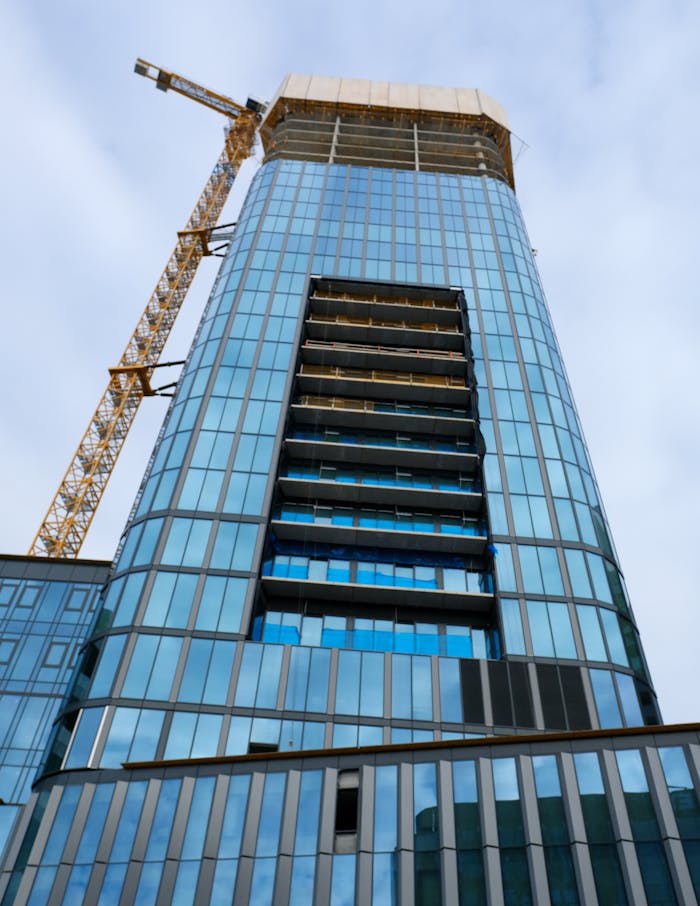 services-02 Glass skyscraper with construction crane against a blue sky, showcasing modern architecture.