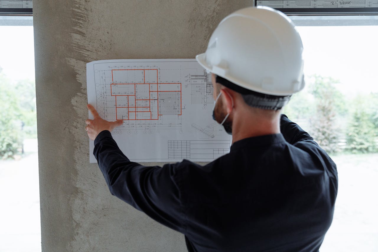 about-01 Engineer in hardhat reviewing architectural floor plans at construction site.