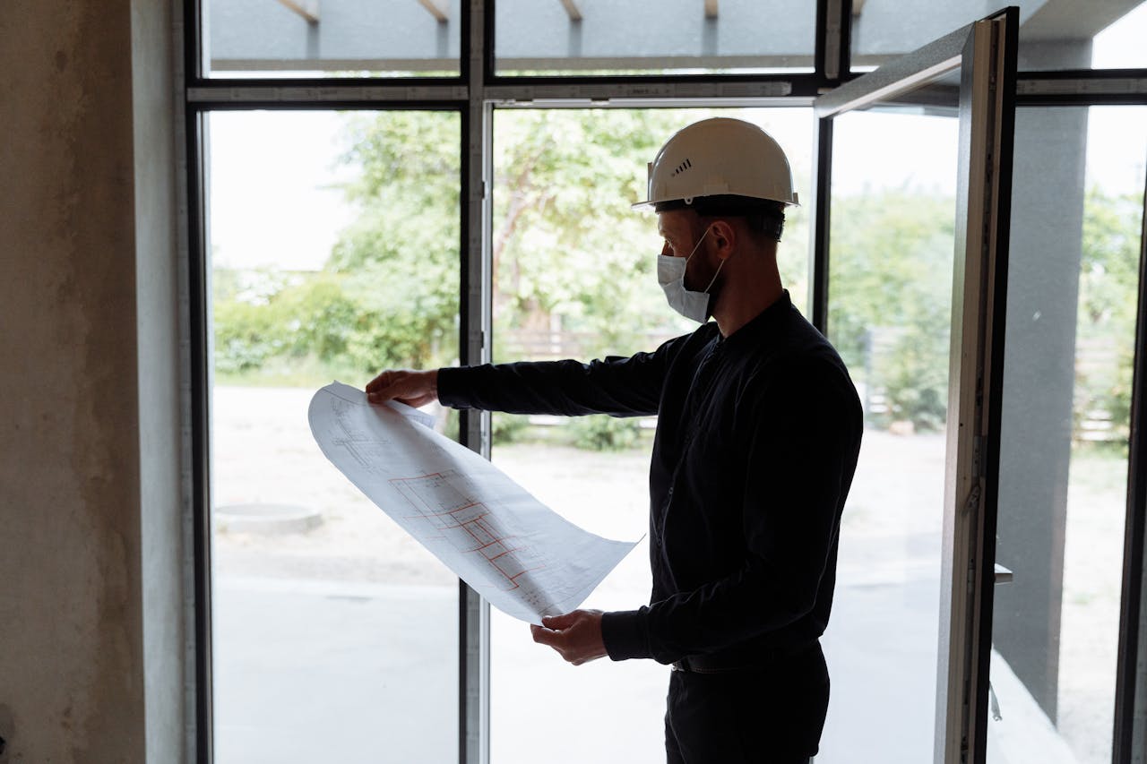 gallery-3 Architect reviewing floor plans indoors, wearing safety gear, focused on construction planning.